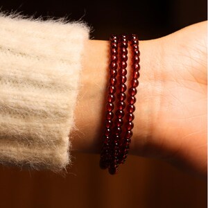 May include: A red beaded bracelet with multiple strands of small, round beads. The bracelet is worn on a person's wrist.