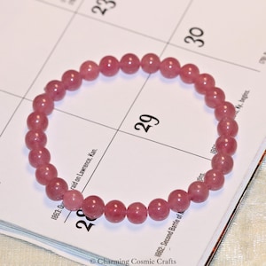 May include: A pink gemstone bracelet with 18 beads. The bracelet is lying on a calendar page with the number 29 visible.