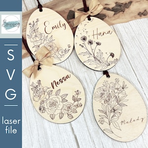 May include: Four wooden oval ornaments with floral designs and names: Emily, Hana, Nessa, and Melody. Each ornament has a brown ribbon for hanging and a decorative bow. The ornaments are laser cut with intricate floral patterns.