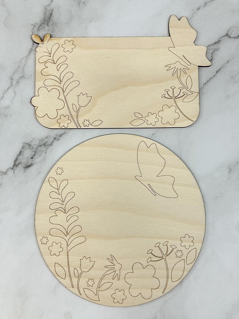 May include: Two unfinished wooden craft shapes: a rectangle and a circle. Both are decorated with etched floral and butterfly designs. The rectangle has a butterfly cutout on one corner. The circle features a butterfly and floral border.