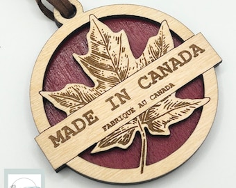 Pode incluir: Um ornamento de madeira cortado a laser com um design de folha de bordo e o texto "MADE IN CANADA FABRIQUE AU CANADA".