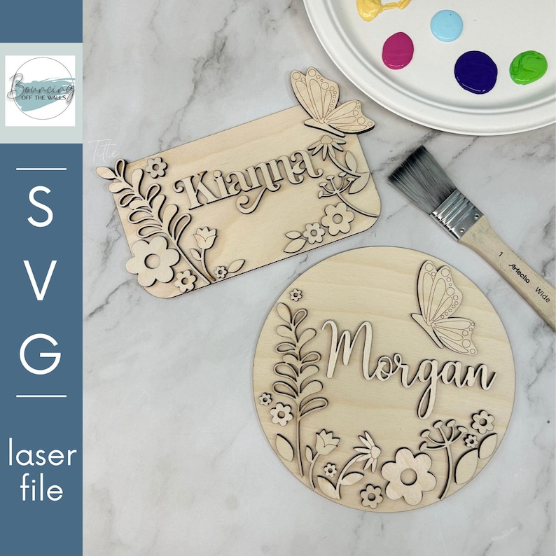 May include: Two laser-cut wooden name signs, one rectangular and one circular, with floral and butterfly designs. The rectangular sign reads "Kianna," and the circular sign reads "Morgan." A paintbrush and a paint palette with various colors are also visible.