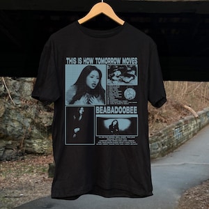 Peut inclure: T-shirt noir avec un imprimé graphique d'une femme et d'une horloge. Le texte "This is how tomorrow moves" et "BEABADOOBEE" est imprimé sur le t-shirt.