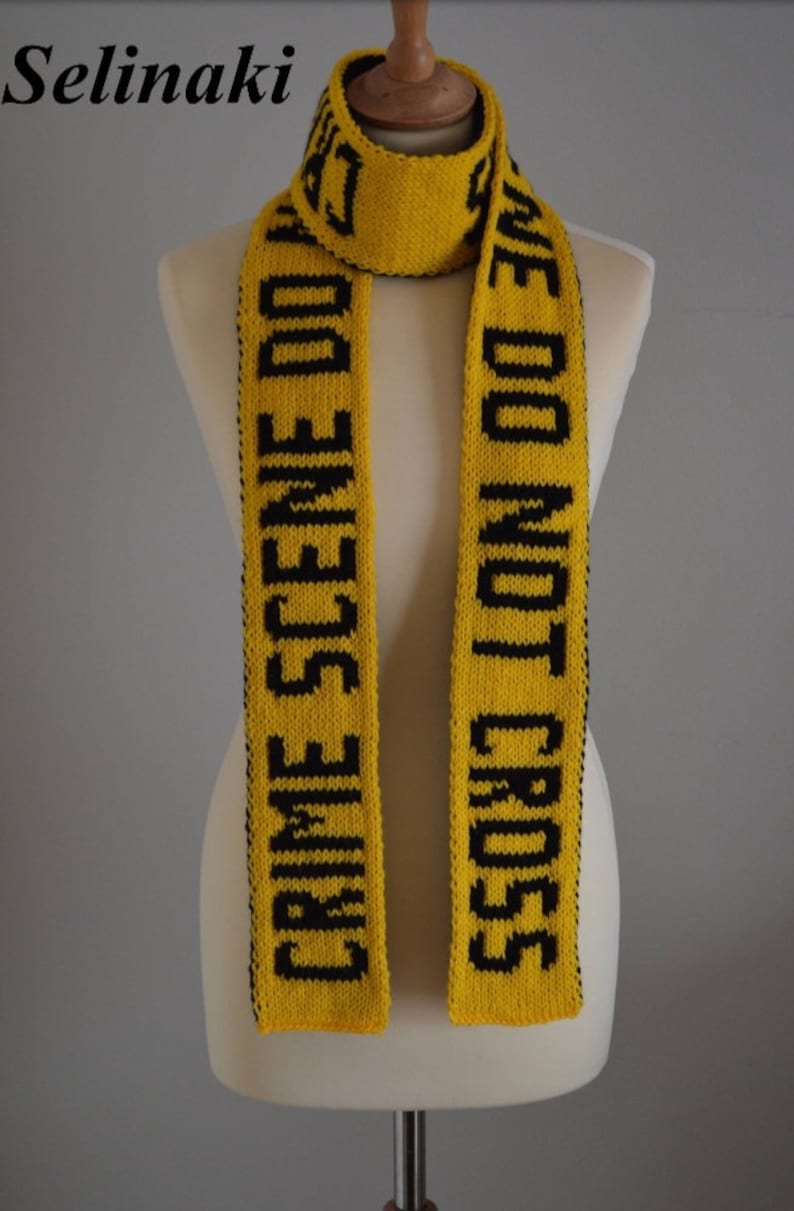 May include: A yellow knitted scarf featuring the black text CRIME SCENE DO NOT CROSS repeated along its length. The scarf is displayed on a mannequin, showcasing the bold contrast between the bright yellow yarn and the dark lettering.