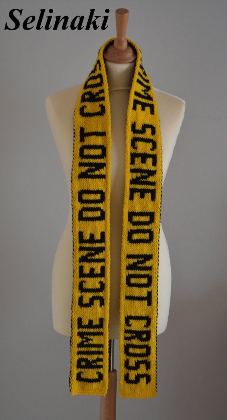 May include: A yellow knitted scarf featuring the black text CRIME SCENE DO NOT CROSS repeated along its length. The scarf has a textured knit pattern with black edges and is displayed on a mannequin. The word Selinaki is printed in the top left corner.
