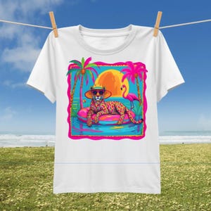 Puede incluir: Una camiseta blanca con un gráfico colorido de un leopardo con sombrero y gafas de sol, descansando sobre un flotador rosa en el agua. La escena incluye palmeras, un sol naranja brillante y un flamenco rosa sobre un fondo azul.