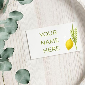 Puede incluir: Una tarjeta rectangular blanca con el texto "YOUR NAME HERE" en verde. Una ilustración de acuarela de un limón amarillo y trigo verde está en el lado derecho de la tarjeta. Hojas de eucalipto en la esquina superior izquierda.