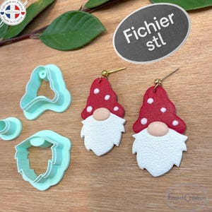 Puede incluir: Pendientes de gnomo con sombreros rojos y barbas blancas, junto con cortadores de arcilla polimérica azul claro. Los pendientes tienen ganchos dorados. También se muestra el texto "Fichier stl".