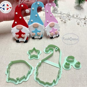 May include: Three felt gnome ornaments with stars, one red, one blue, and one pink.  The ornaments are hanging from a string.  The image also shows three cookie cutters: a star, a gnome, and two circles.