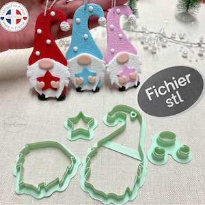 Peut inclure: Trois ornements de gnome en feutre rouge, bleu et rose, chacun avec une barbe blanche et une étoile. En dessous, des emporte-pièces en plastique vert en forme d'étoile, de chapeau de gnome et de visage de gnome. Le texte "Fichier stl" est sur un ovale gris.