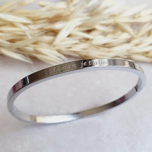 Puede incluir: Un brazalete de plata con la inscripción "Maman je t'aime" grabada en el exterior.