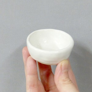 Op de afbeelding: Een kleine, witte keramische kom met een licht afgeronde bodem. De kom is glad en heeft een eenvoudig, elegant ontwerp.
