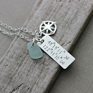 May include: Silver necklace with a compass charm, a small piece of sea glass, and a tag with the coordinates "48°13'11" N 122°41'10" W" engraved on it.