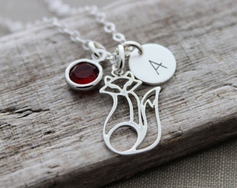 May include: Silver necklace with a red gemstone, a fox charm, and a personalized initial charm with the letter "A".