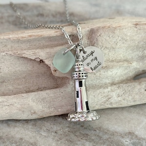 May include: Silver necklace with a lighthouse charm and a sea glass bead. The charm has the words "always in my heart" engraved on it.