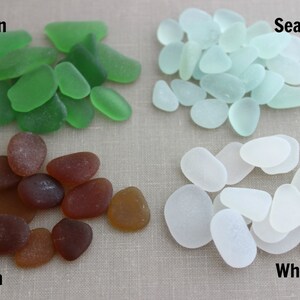 May include: Four piles of sea glass in different colors: green, seafoam, brown, and white. The sea glass is arranged in a square pattern on a light brown surface.