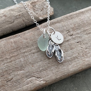 May include: Silver necklace with a charm of a sea glass, flip flops, and a letter K.