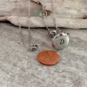 May include: Silver lighthouse pendant necklace with a small sea glass charm. The pendant has an inscription that reads "Always in my heart". The necklace is shown with a penny for size comparison.
