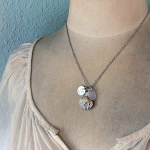 May include: A silver chain necklace with a seashell charm, a small round charm with the text "Always in my heart", and a clear glass charm.