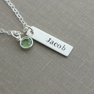 May include: Silver necklace with a bar pendant engraved with the name "Jacob" and a small green gemstone charm.