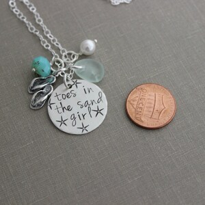 May include: Silver necklace with a charm that says "toes in the sand girl" with a turquoise stone, a white pearl, and a sea glass charm. The necklace is about the size of a US penny.