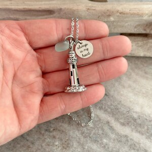 May include: Silver necklace with a lighthouse charm and a round charm that says "always in my heart". The necklace also features a small piece of sea glass.