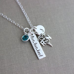 May include: Silver necklace with a teal blue gemstone, a charm with the word "RN" and a medical symbol, and a bar charm with the text "live.love.heal".