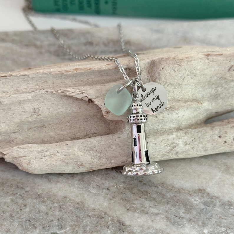 May include: Silver necklace with a lighthouse charm and a sea glass bead. The charm has the words "always in my heart" engraved on it.