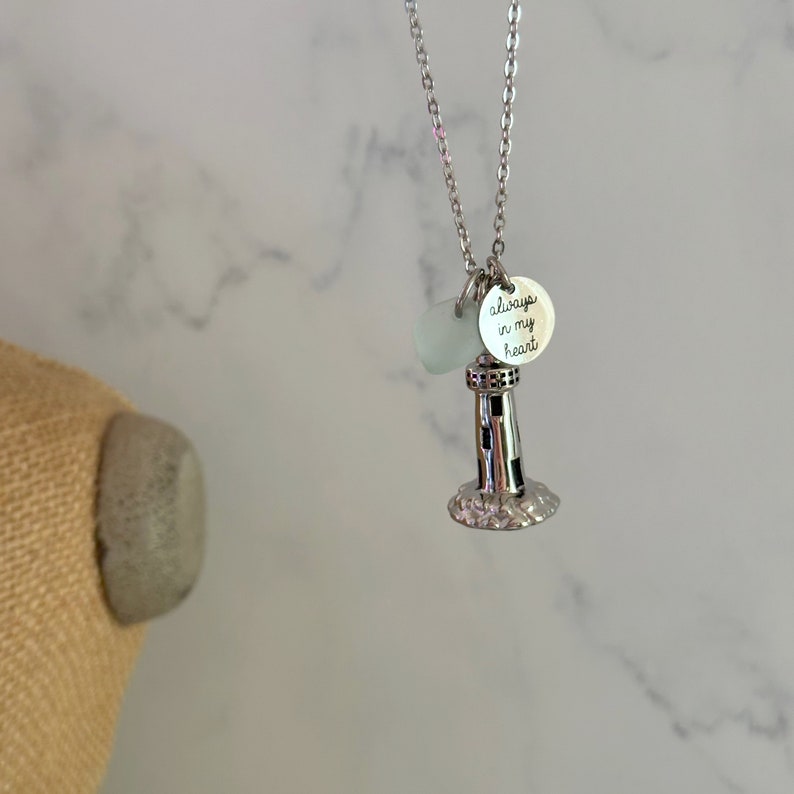May include: Silver necklace with a lighthouse charm and a small round charm that says "always in my heart".