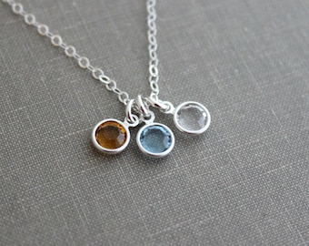 May include: A silver necklace with three small charms, each featuring a different colored gemstone. The charms are a light blue, a clear, and an amber color.