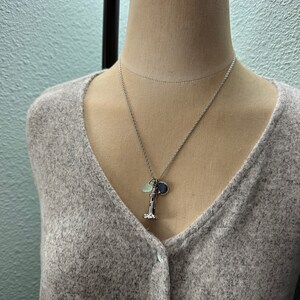 May include: A silver necklace with a lighthouse charm, a small blue charm, and a light green charm.
