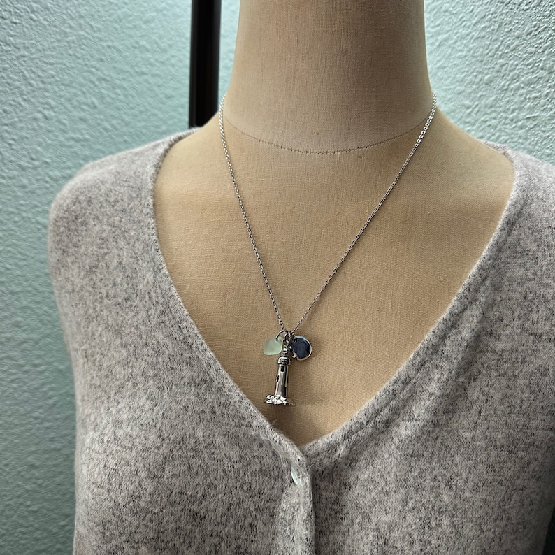 May include: A silver necklace with a lighthouse charm, a small blue charm, and a light green charm.