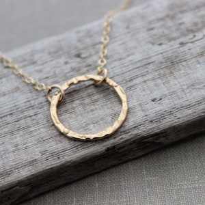 May include: A delicate gold necklace with a hammered circle pendant. The necklace is on a wooden surface.