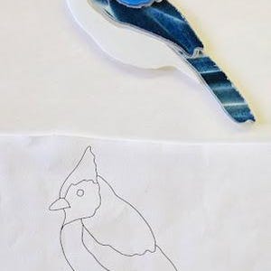 May include: A blue jay bird figurine with a white body, blue head crest, and dark blue wing and tail details. Below it is a line drawing of the same bird.