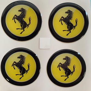 Könnte beinhalten: Vier runde schwarze und gelbe Aufkleber mit einem schwarzen Pferdelogo. Das Pferd bäumt sich auf seinen Hinterbeinen auf, die Vorderbeine in der Luft. Das Pferd blickt zur linken Seite des Aufklebers. Die Aufkleber befinden sich auf einem weißen Hintergrund.