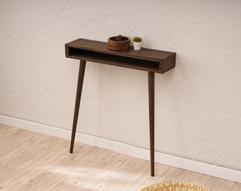 May include: A dark brown wooden console table with a shelf and tapered legs. The table is decorated with a small wooden bowl and a potted plant.