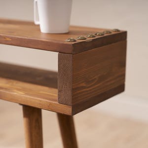 May include: A wooden side table with a shelf and three legs. The table has a dark brown stain and is decorated with metal studs.