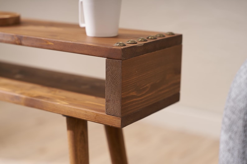 May include: A wooden side table with a shelf and three legs. The table has a dark brown stain and is decorated with metal studs.