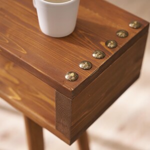 May include: A wooden side table with a brown stain and decorative brass accents. The table has a shelf and a top surface.