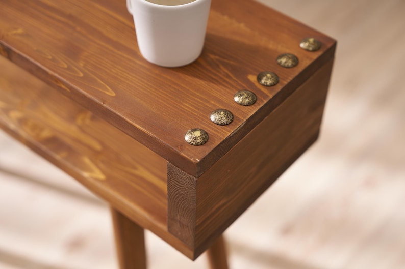 May include: A wooden side table with a brown stain and decorative brass accents. The table has a shelf and a top surface.