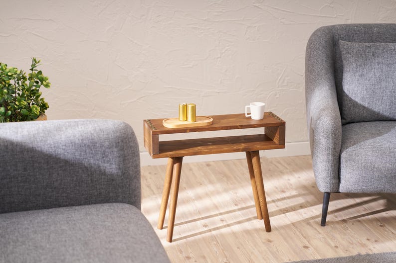 May include: A wooden side table with a shelf and four legs. The table is brown and has a white ceramic mug and three gold metal containers on top.