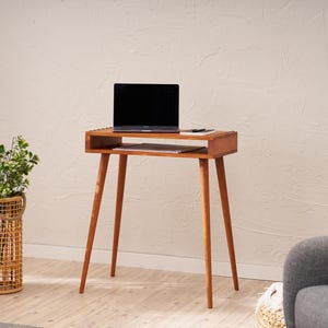 May include: A mid-century modern style wooden side table with a laptop on top. The table has a rectangular top with a lower shelf and four angled legs. The laptop is black, and the table is a warm brown color. The table is approximately 30 inches tall.