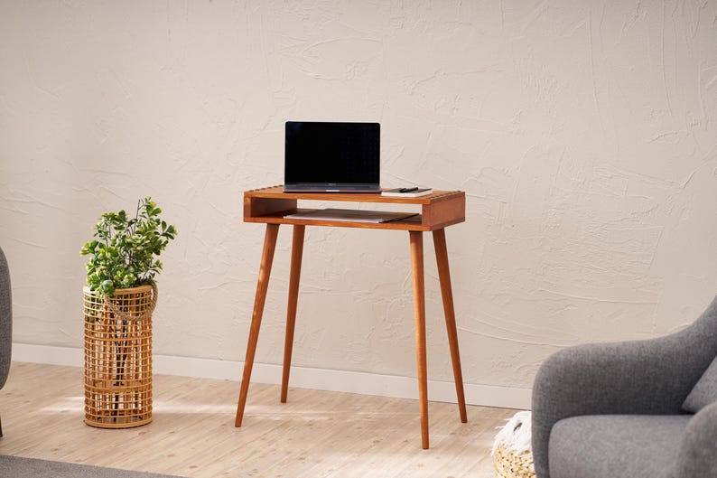 May include: A mid-century modern style wooden side table with a laptop on top. The table has a rectangular top with a lower shelf and four angled legs. The laptop is black, and the table is a warm brown color. The table is approximately 30 inches tall.