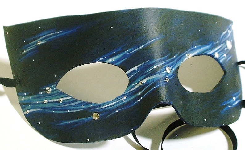 May include: A black leather masquerade mask with a blue and white starry night design. The mask has two eye holes and a black ribbon tie.