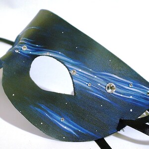 May include: A black leather masquerade mask with a blue and white starry night design. The mask has a single eye hole and is decorated with rhinestones.