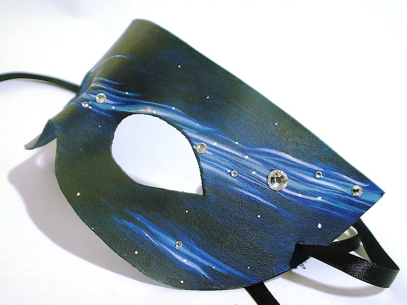May include: A black leather masquerade mask with a blue and white starry night design. The mask has a single eye hole and is decorated with rhinestones.