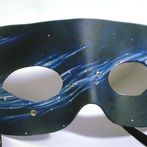 May include: A black leather masquerade mask with blue and white painted designs and silver rhinestones. The mask has two eye holes and a black ribbon tie.