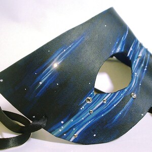 May include: A black leather masquerade mask with a blue and white starry night design. The mask has a single eye hole and is decorated with rhinestones.