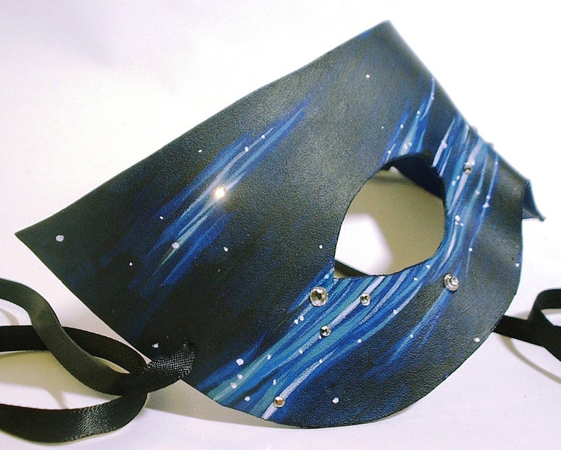 May include: A black leather masquerade mask with a blue and white starry night design. The mask has a single eye hole and is decorated with rhinestones.