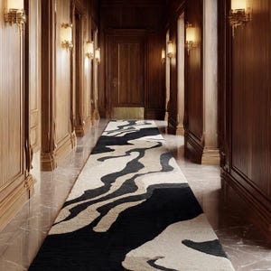 May include: A long, rectangular rug with a black and beige abstract design. The rug is placed in a hallway with wood-paneled walls and a marble floor. Wall sconces provide warm lighting.